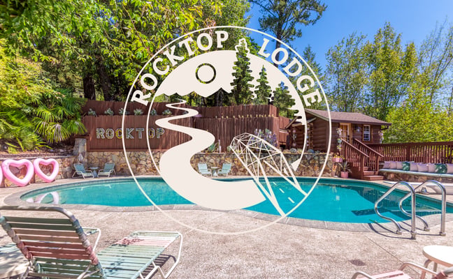 Rocktop Lodge sign with turquoise swimming pool, lounge chairs, log cabin, and pine trees in background